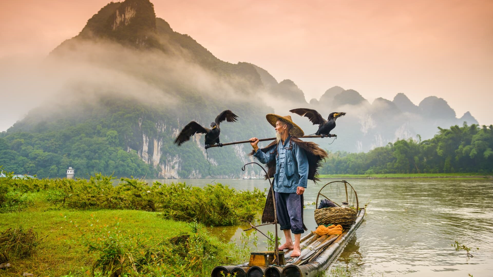 A cormorant fisherman on a bamboo raft on the Li River below mist-covered karst peaks