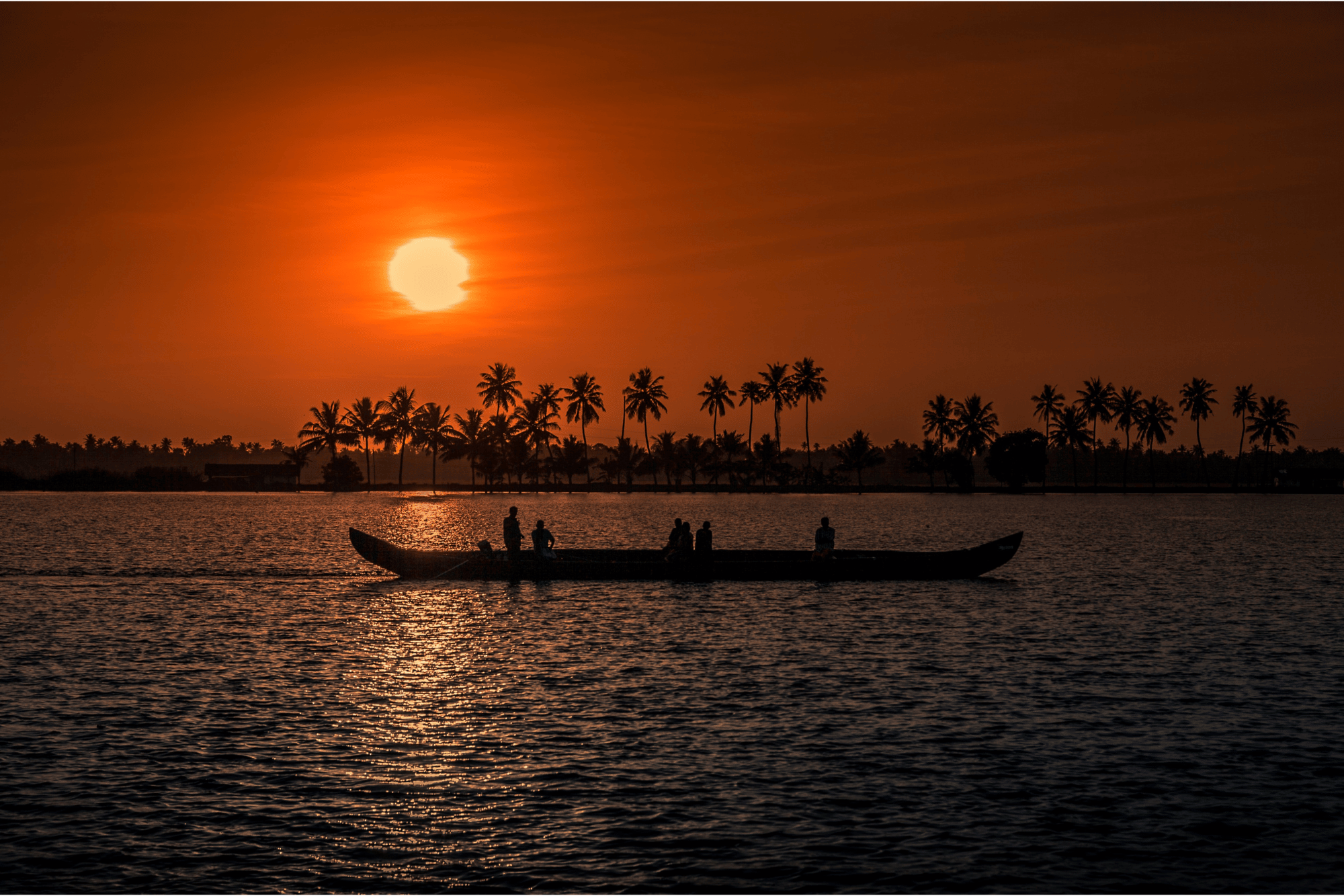 Sunset over a Kerala waterway with a boat and palm trees