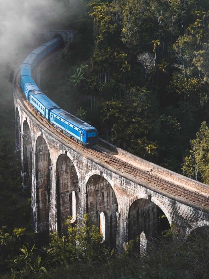 The blue train crossing the Nine Arch Bridge through misty hill-country forest