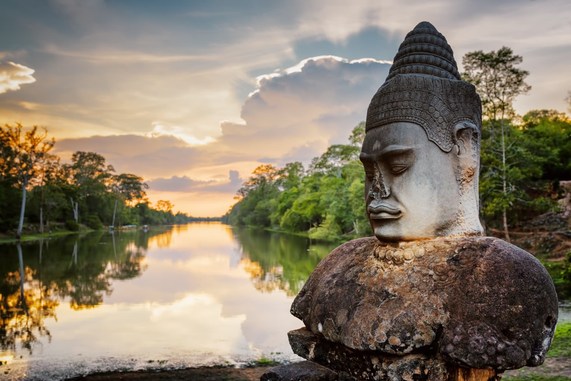 Ancient stone guardian beside calm water at sunset in Vietnam
