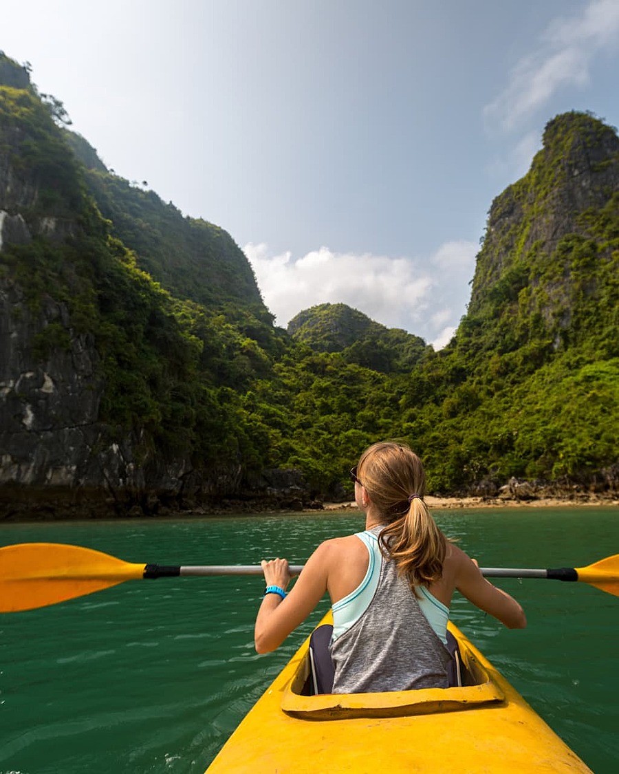 A kayaker paddling through emerald water towards towering limestone islands