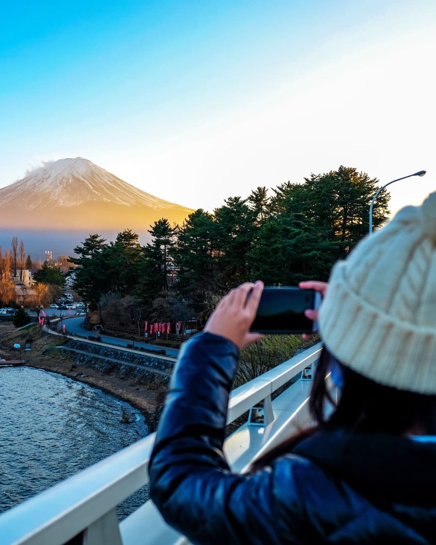 A traveller photographing Mount Fuji at sunrise from a bridge over Lake Kawaguchi