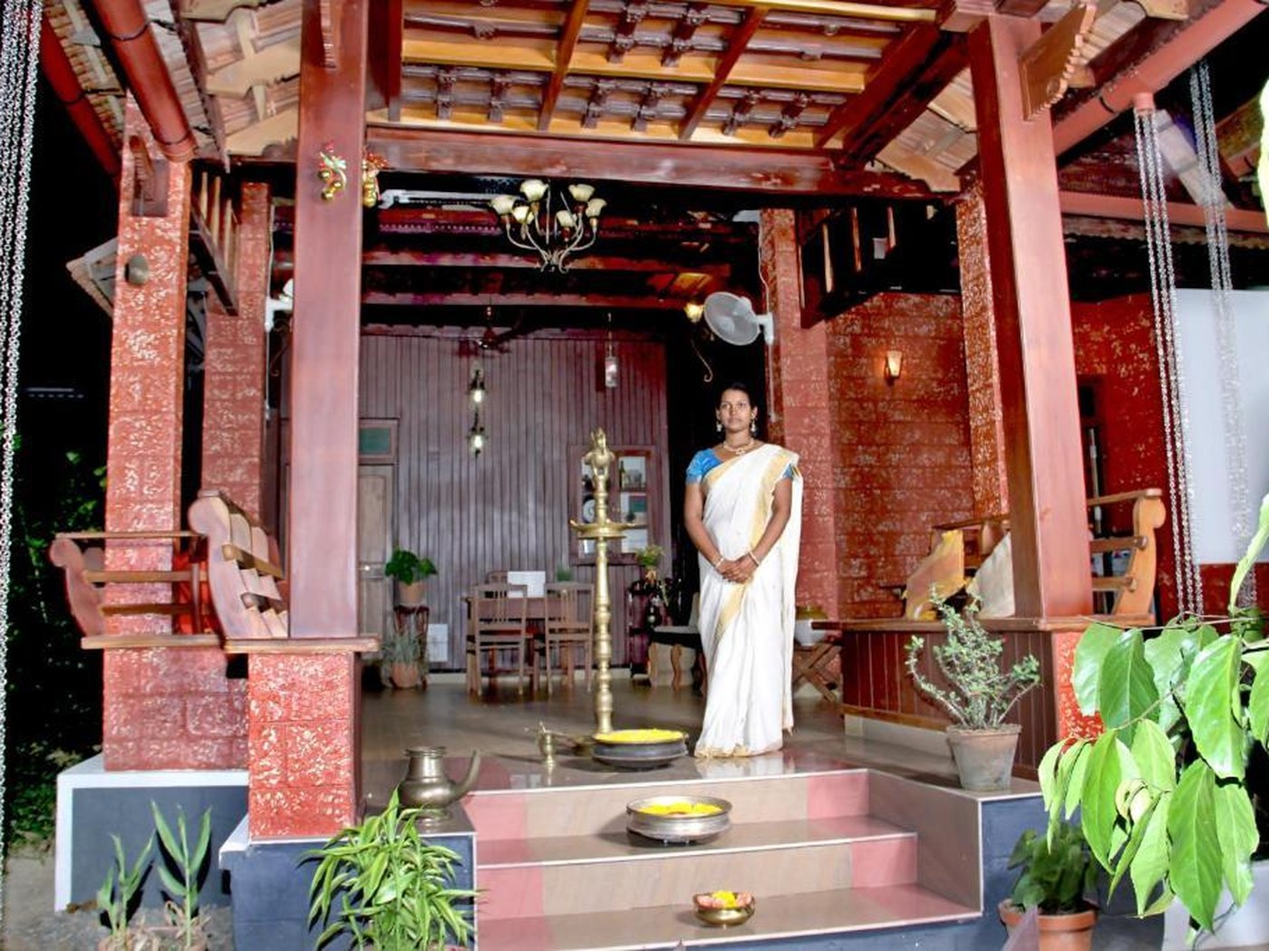 Lit entrance porch with a brass lamp and host at Mannaas Veedu Homestay