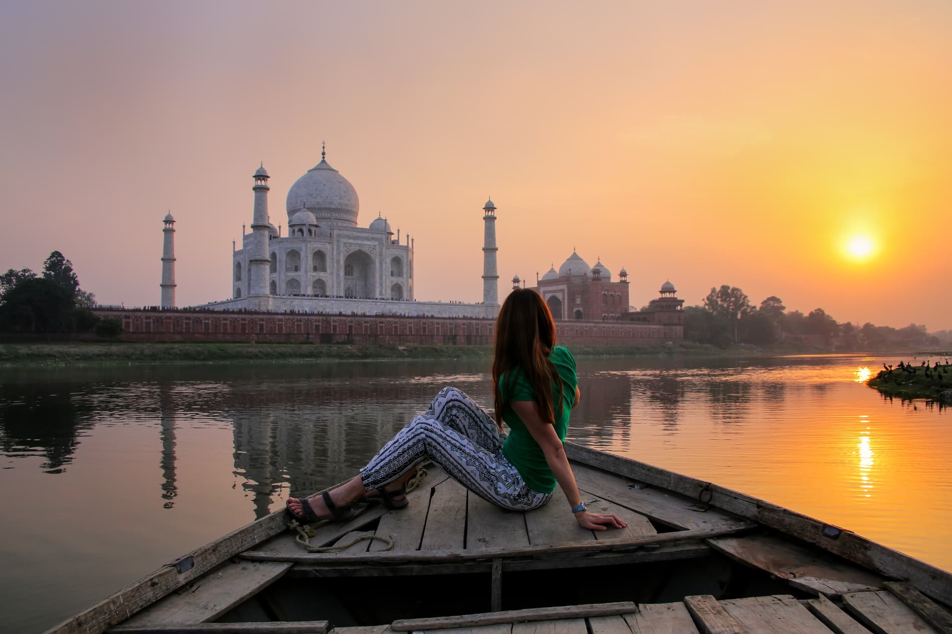 A couple in a boat watching the Taj Mahal glow at sunset on an India honeymoon tour