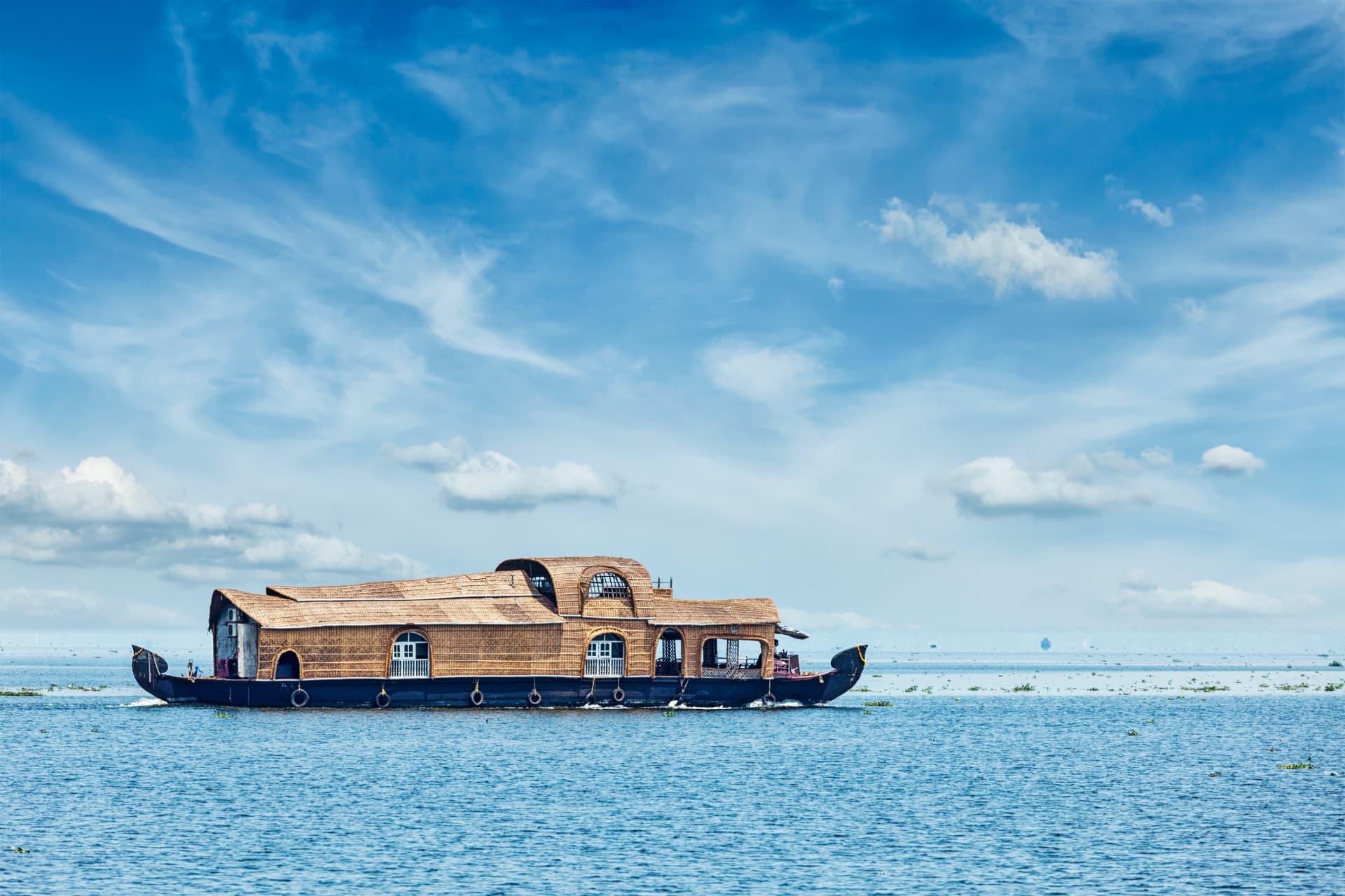 A traditional Kerala houseboat on open water under a blue sky