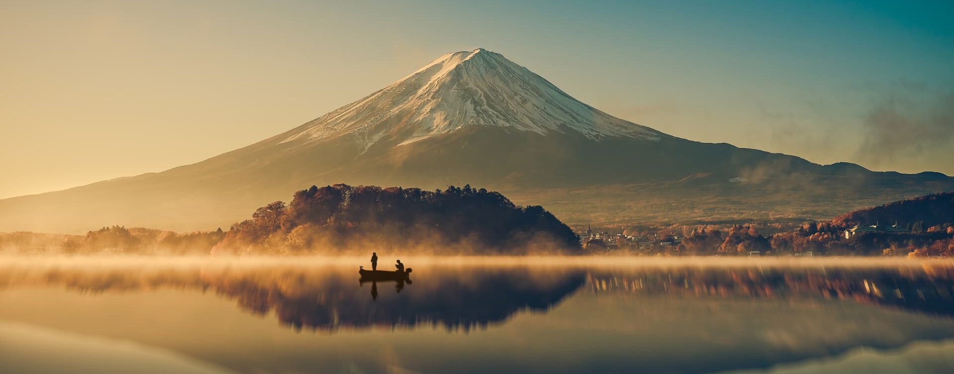 Mount Fuji reflected in a misty lake at dawn, with a small boat on the water